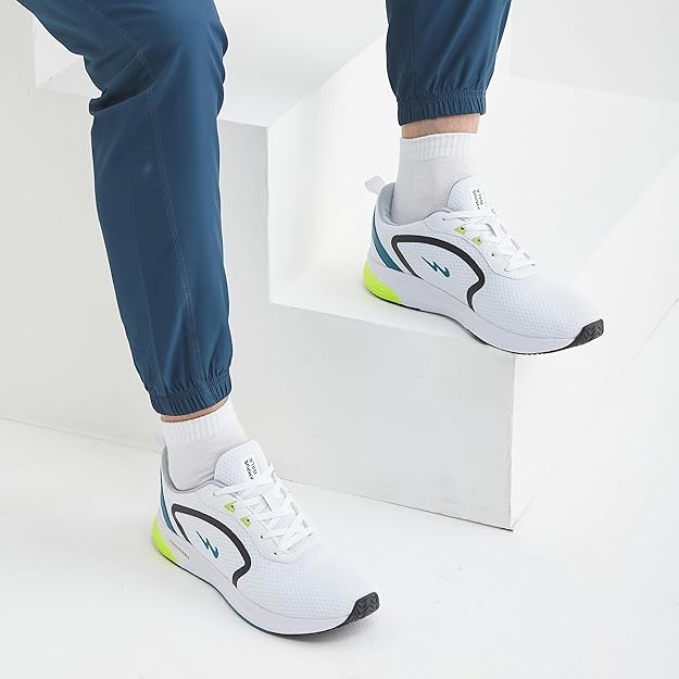 White sneakers with black and green accents worn by a person sitting on a white box.