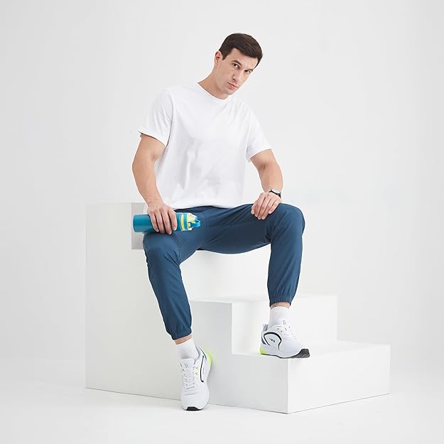 Man sitting on a white cube holding a blue bottle, wearing a white t-shirt, blue pants, and white sneakers.