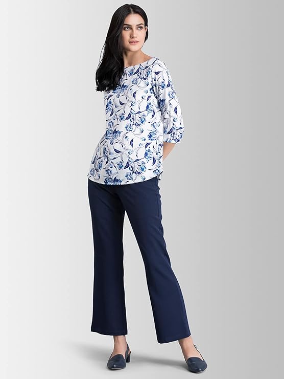 Woman wearing a floral blouse and navy pants on a gray background