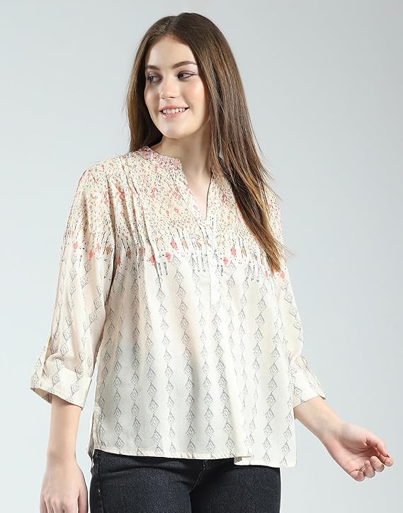 Woman wearing a light-colored patterned blouse against a plain background